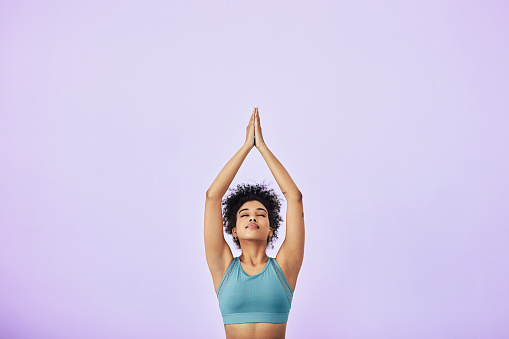 Studio shot of a fit young woman meditating against a purple background