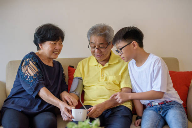 счастливая азиатская старшая пара принимая кровяное давление в живущей комнате - blood pressure gauge surveillance home interior house стоковые фото и изображения