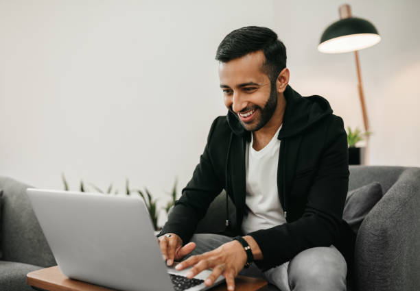 Trendy handsome Gen z Indian arabic man working on laptop in waiting area, Smiling and staring at screen Trendy handsome Gen z Indian arabic man working on laptop in waiting area, Smiling and staring at screen south asia stock pictures, royalty-free photos & images