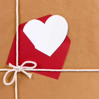 Valentines day gift with white heart shape card, red envelope, brown paper package parcel background