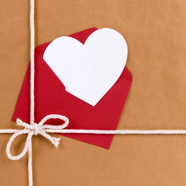 Valentines day gift with white heart shape card, red envelope, brown paper package parcel background stock photo