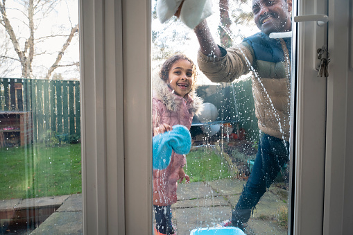 Daughter helping her father playing with water while cleaning their home windows.