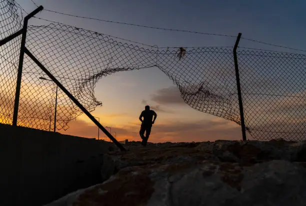 Refugee man running behind fence,