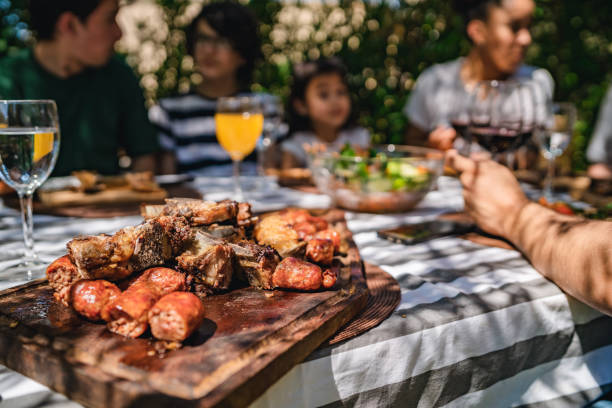 Traditional  Asado Midday Meal for Argentine Family Smiling family members sitting at outdoor dining table and enjoying grilled meat, sausages and vegetables for weekend midday meal. Asado concept. argentinian culture stock pictures, royalty-free photos & images