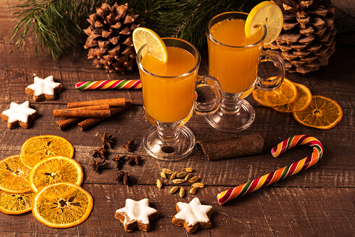 Christmas drink and candy cane, pines, orange chips, spices on wooden table.
