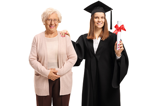 Female graduate with bachelor degree in a graduation gown posing with her grandmother isolated on white background