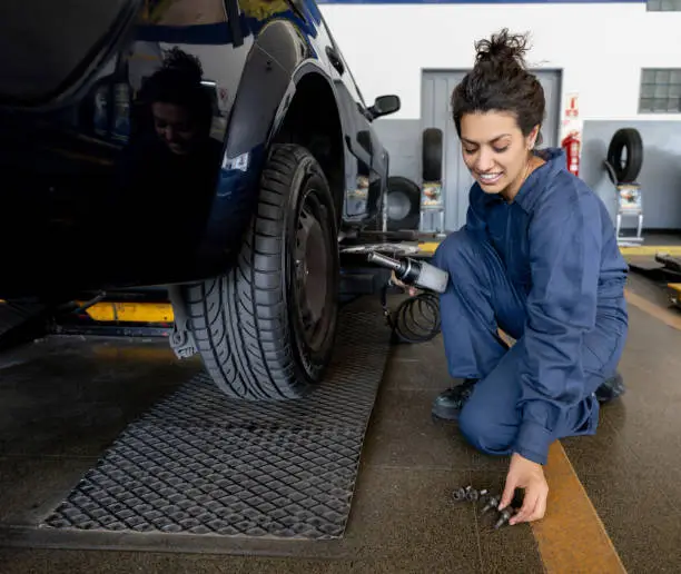 Cheerful female mechanic changing a tire at an autorepair shop - Service concepts