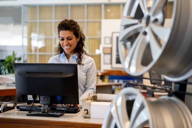 mulher bonita que trabalha na recepção de uma loja de reparo de automóvel que olha a tela de computador muito alegre - car for sale - fotografias e filmes do acervo