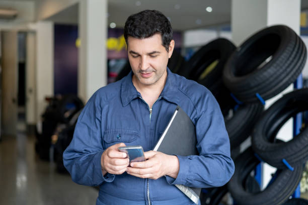 istock Cheerful mechanic taking a break at the car workshop texting on smartphone 1193706159