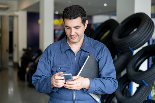 Cheerful mechanic taking a break at the car workshop texting on smartphone - Business industry concepts