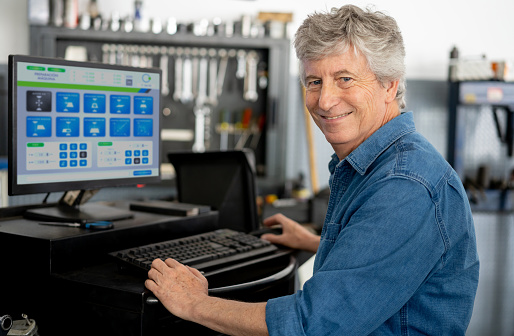 Portrait of business owner of a car alignment shop smiling at camera standing next to computer screen - Service concepts **DESIGN ON SCREEN WAS MADE FROM SCRATCH BY US**