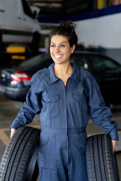 bella meccanica donna che trasporta pneumatici nuovi per un'auto in un'officina di auto sorridente - auto repair shop tire car mechanic foto e immagini stock