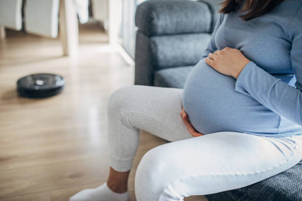 istock Pregnant lady sitting on sofa while robot vacuum cleaner is cleaning 1193708889
