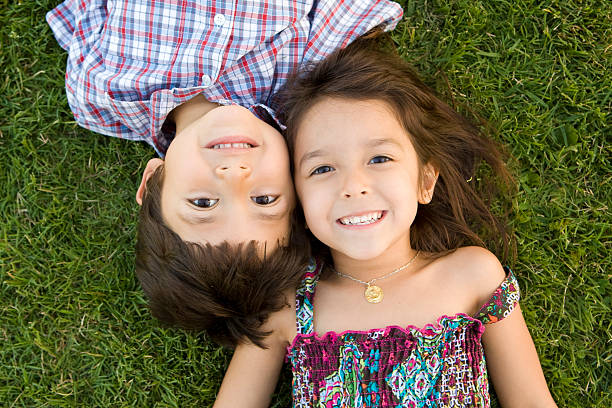 two young siblings lying on the grass smiling together - broer en zus stockfoto's en -beelden