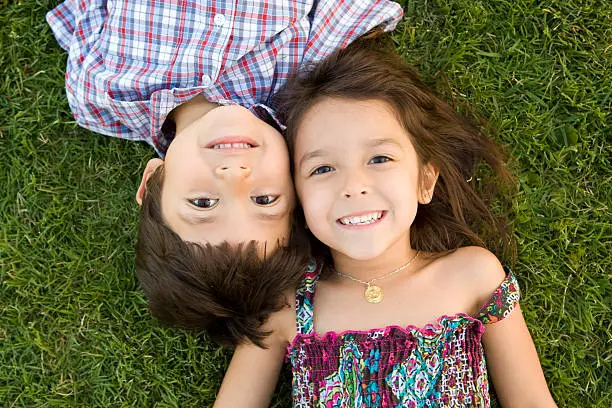 Photo of Two young siblings lying on the grass smiling together