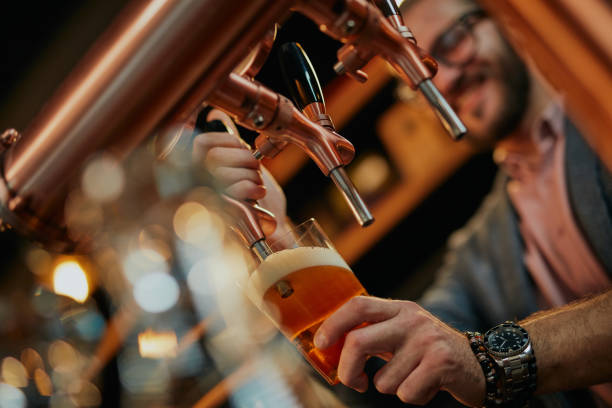 Primo tempo di un bel barista barbuto caucasico in piedi al bar e che versa birra dal rubinetto. - foto stock