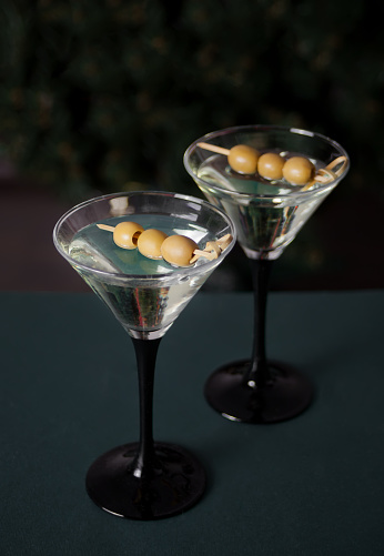 Two glasses of martini with olives on the dark background