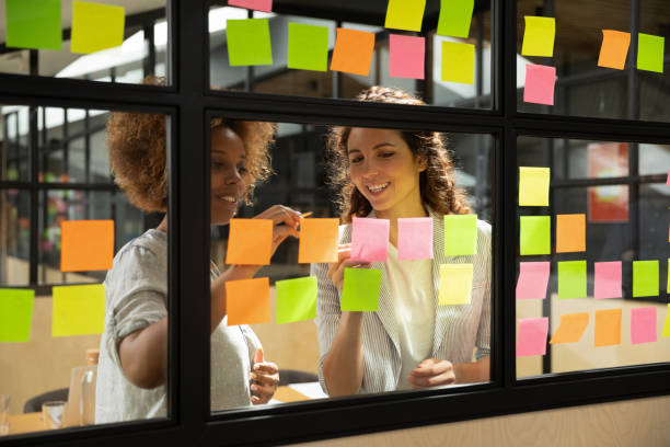 Smiling african american scrum mater working with colleague. Smiling african american scrum mater working with happy caucasian pleasant colleague, improving IT business project workflow on glass window kanban agile brainstorming board at modern office. scrum stock pictures, royalty-free photos & images