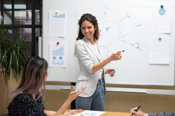 uśmiechnięta millenialska kaukaska liderka zespołu odpowiadająca na pytania azjatyckiego kolegi. - presenter young adult women marketing zdjęcia i obrazy z banku zdjęć