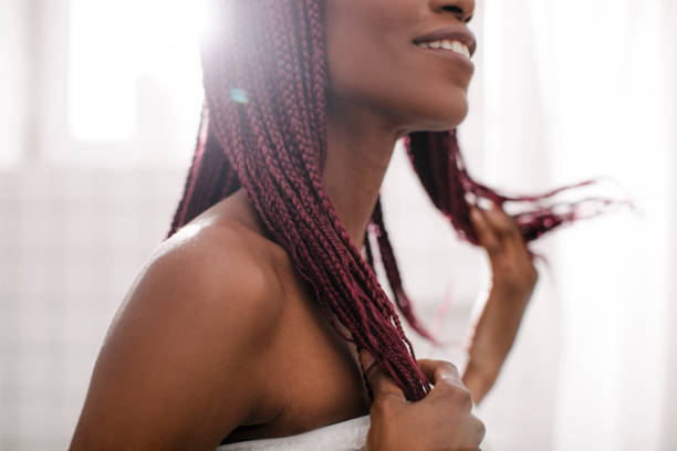 A Woman Holding her Hair Brides Beautiful smiling African woman standing at bathroom and holding her braided hair. black woman hair braids stock pictures, royalty-free photos & images