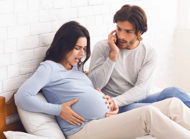 Pregnant Woman Having Contractions, Her Panicked Husband Calling Doctor Time To Give Birth. Pregnant Woman Having Contractions At Home, Her Panicked Husband Calling Doctor, Free Space muscular contraction stock pictures, royalty-free photos & images