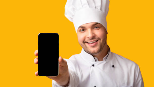 istock Chef Showing Phone Blank Screen Standing On Yellow Studio Background 1193721946