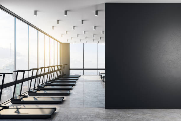 istock Blank black wall in modern loft style gym with black treadmills at sunset. 1193724331