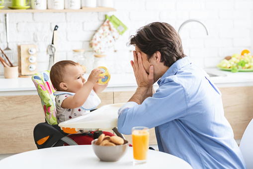 Peekaboo. Cheerful daddy playing with cute baby son in kitchen interior, empty space
