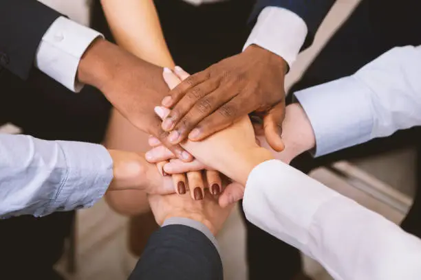 Photo of Multiethnic corporate teame stacking hands together in office