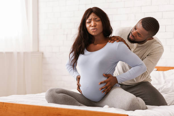 Pregnant lady suffering from backache, husband massaging her shoulders Pregnant black lady suffering from back pain, sitting on bed, her attentive husband massaging her shoulders, free space black male massage stock pictures, royalty-free photos & images