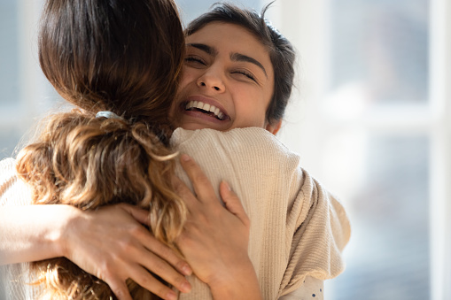 Head shot close up happy mixed race girl cuddling smiling indian female friend. Overjoyed excited best buddies emracing hugging, greeting each other with success, true strong friendship concept.