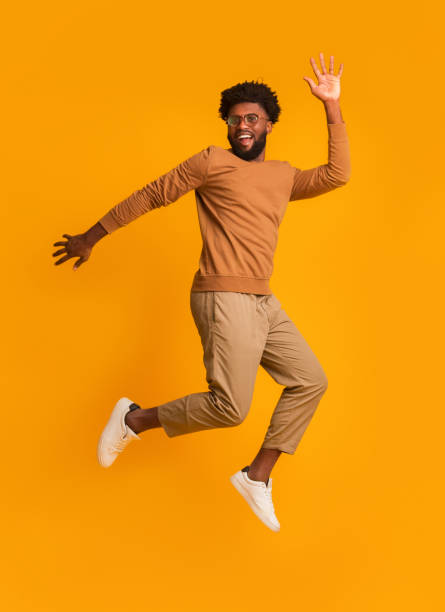 istock Cheerful guy in glasses jumping over orange background 1193735069