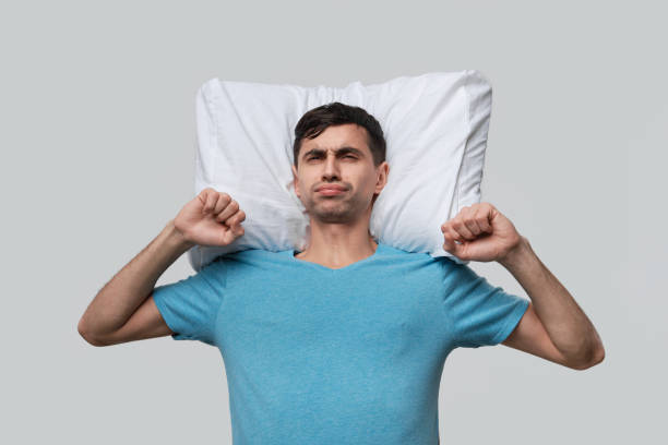 istock Tired brunet man in a blue tee resting on a white pillow isolated over grey background. 1193735733