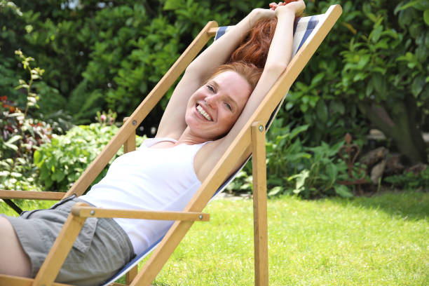 mujer pelirroja disfruta del verano en el sofá jardín a rayas - deck chair summer grass outdoor chair fotografías e imágenes de stock