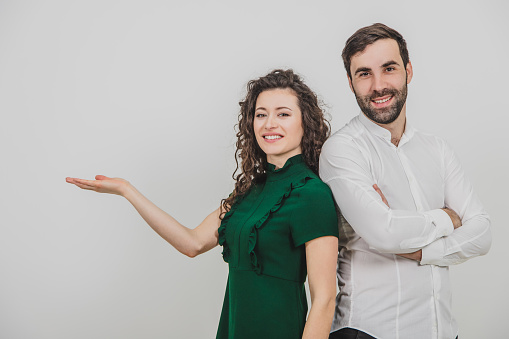Group of two people on white background standing back to back, man folded hands, woman pointing her hand to the side,