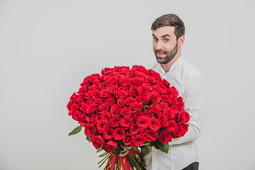 St. Valentine's Day concept. Elegant bearded man holding a bouquet of red roses for valentines day, isolated on white background.