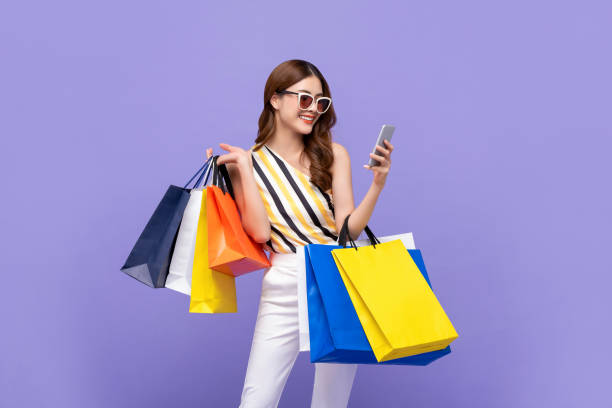 bella donna asiatica che porta borse colorate che fanno shopping online con il telefono cellulare - sunglasses women smiling portrait foto e immagini stock