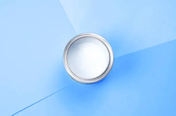 Photo of Open can of white paint on a blue background.