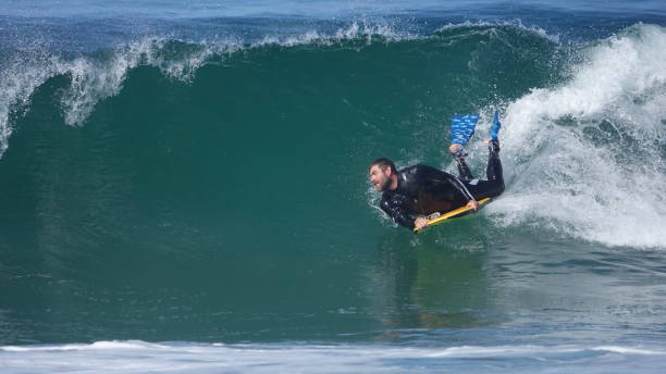 Man surfing on a boogie board. A middle-aged man (possibly young end of baby-boomer generation) with a beard is surfing a large wave on a yellow boogie board. He is wearing a wetsuit and is using fins. body board stock pictures, royalty-free photos & images