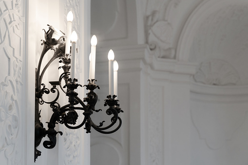 side view closeup of black cast iron vintage wall lamp with candlesticks against an elegant ornated white wall