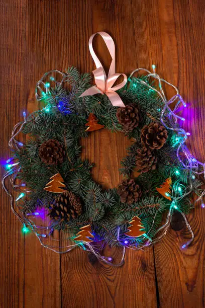 Christmas wreath flatlay. Green spruce branches decorated with orange zest, lights, pine cones and ribbon bow on wooden background,rustic style.New Year 2020 concept.Hand made eco-friendly decorations