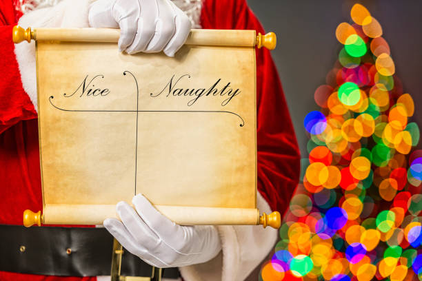 Santa Claus showing a parchment scroll of who is naughty & nice and bokeh from Christmas tree in the background stock photo