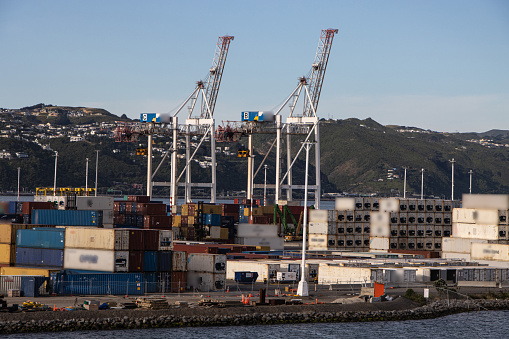 Cranes in container port seen from ferry deck with hills and homes in the background