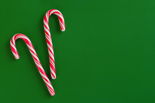 Two christmas red and white candy canes on green paper background. Copy space for text.