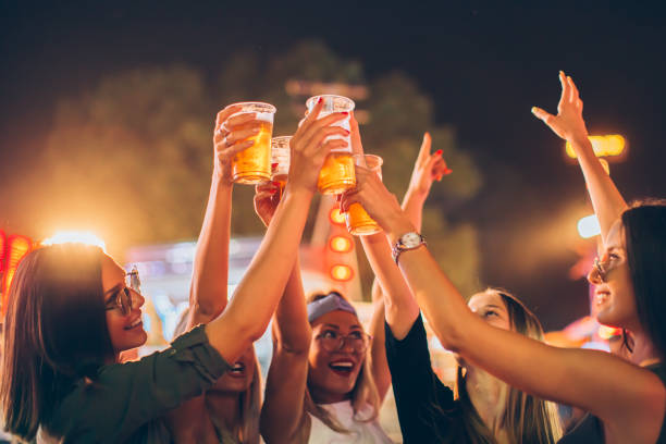 groupe d'amis féminins encourageant avec la bière dans le stationnement d'amusement - music festival park friendship summer photos et images de collection