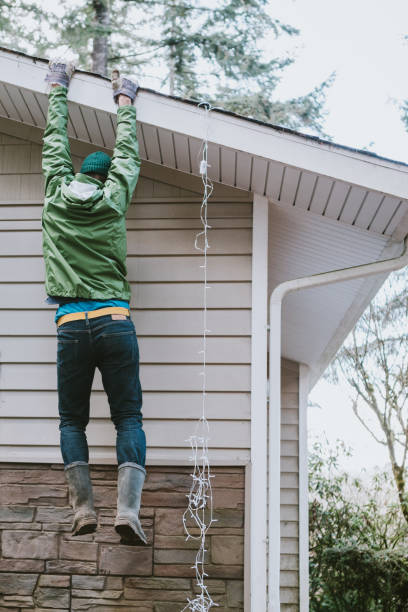 man verliest ladder terwijl opknoping kerstverlichting op huis - hangen stockfoto's en -beelden