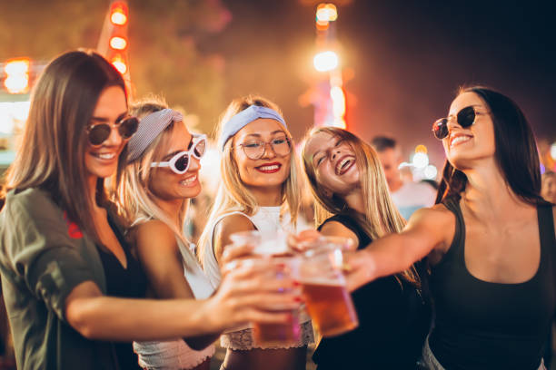 groupe d'amis féminins encourageant avec la bière dans le stationnement d'amusement - music festival park friendship summer photos et images de collection