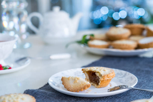 istock Tea time table setting with broken Mince Pie with filling on white plate. Traditional english festive pastry with lightened christmas tree on background. Cozy home mood. Close up, selective focus. 1193786568