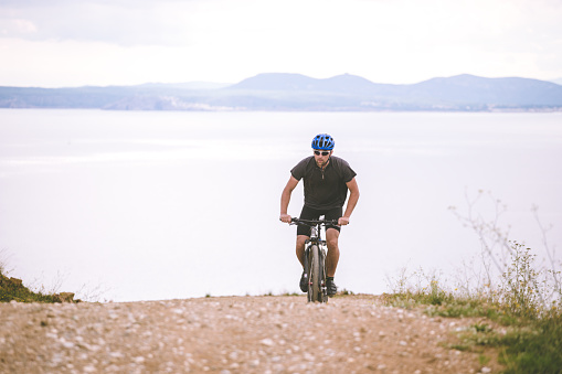 Theme tourism and cycling on mountain biking. guy rides uphill on a rocky, rocky road against the background of the Mediterranean Sea in Spain on the shore of the kosta brava in helmet and sportswear.