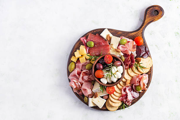 plato de antipasto con jamón, prosciutto, salami, queso, galletas y aceitunas sobre un fondo ligero.  mesa de navidad. vista superior, sobrecarga - cheese wine food appetizer fotografías e imágenes de stock